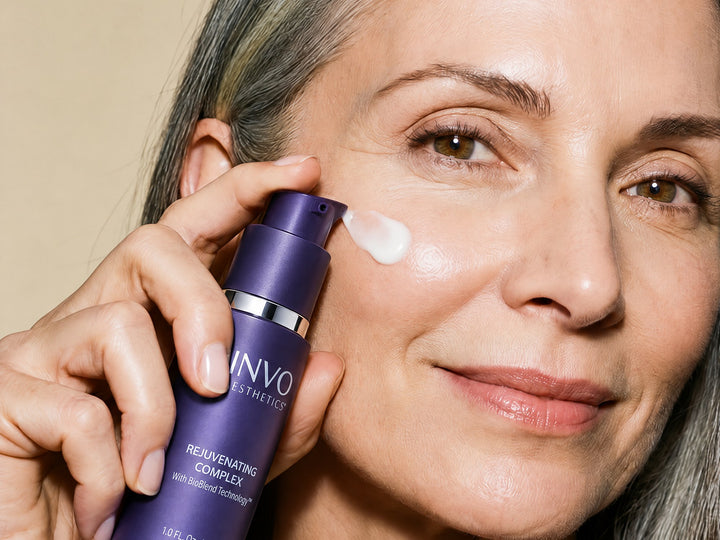 A woman applying INVO Rejuvenating Complex exosome serum along her cheekbone, bottle in hand