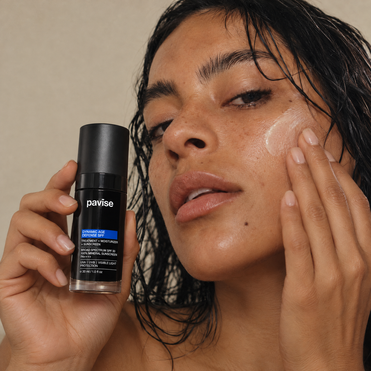 Woman blending Pavise Dynamic Age Defense mineral SPF into her cheek, holding the bottle